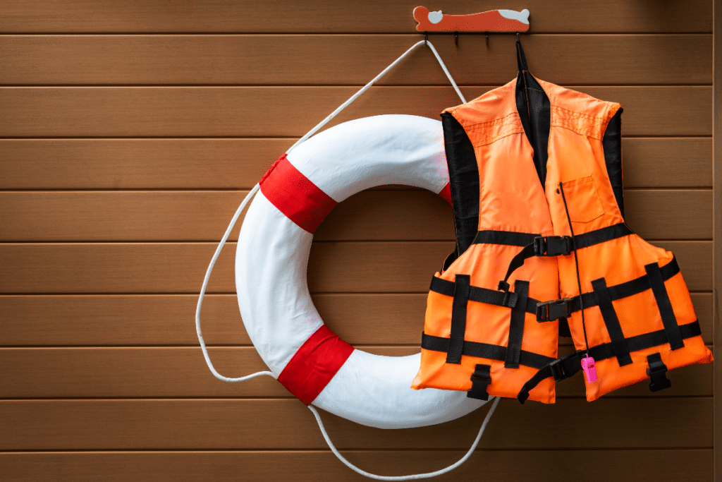 Un gilet de sauvetage orange et un anneau en caoutchouc blanc accrochés sur un mur en bois